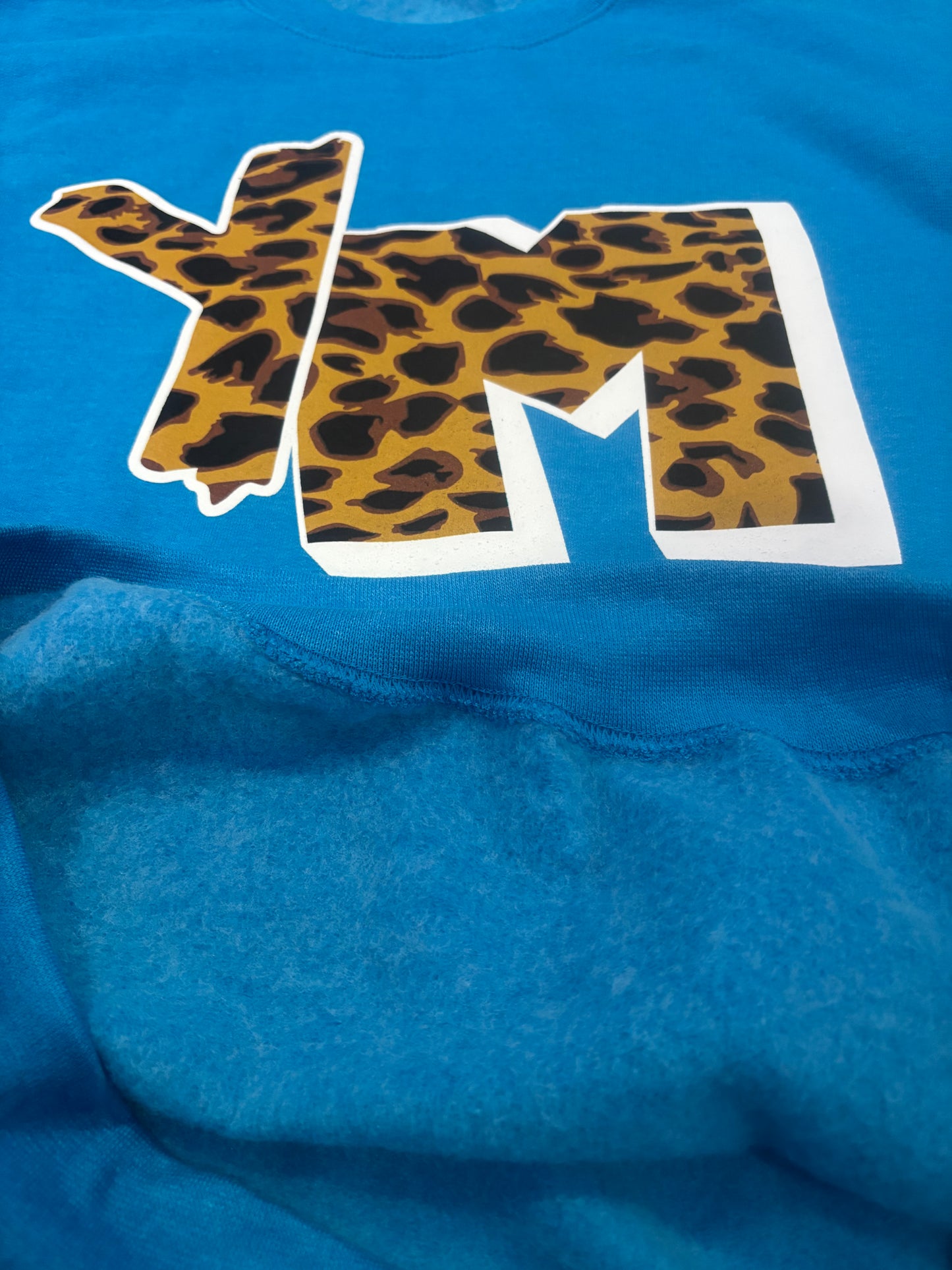 Turquoise sweater with a large white letter 'YM' featuring a leopard print design.