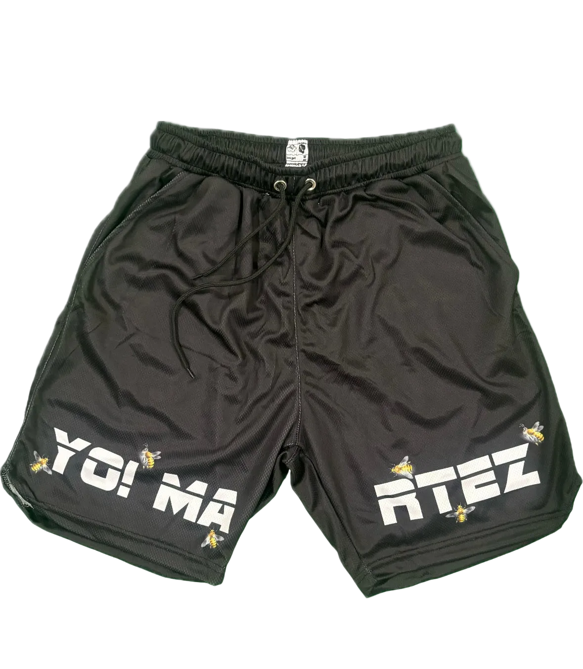 Black athletic shorts with a drawstring waist, featuring 'YO! MA' on the left leg and 'RTEZ' on the right leg in bold white letters, accented with small yellow bee graphics, shown on a plain white background.