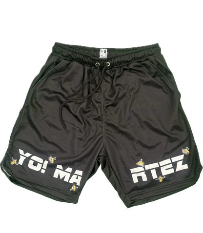 Black athletic shorts with a drawstring waist, featuring 'YO! MA' on the left leg and 'RTEZ' on the right leg in bold white letters, accented with small yellow bee graphics, shown on a plain white background.