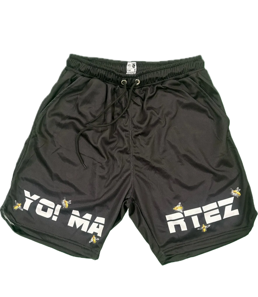 Black athletic shorts with a drawstring waist, featuring 'YO! MA' on the left leg and 'RTEZ' on the right leg in bold white letters, accented with small yellow bee graphics, shown on a plain white background.