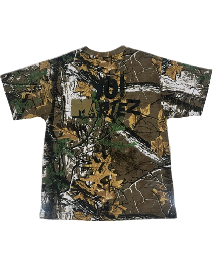 A short-sleeve crewneck t-shirt featuring a brown and green woodland camouflage pattern with a black 'JOL MARTEZ' graphic printed across the chest.