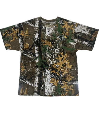 A short-sleeve crewneck t-shirt featuring a realistic woodland camouflage pattern with brown tree trunks, green pine needles, and golden-yellow autumn leaves on a white background.