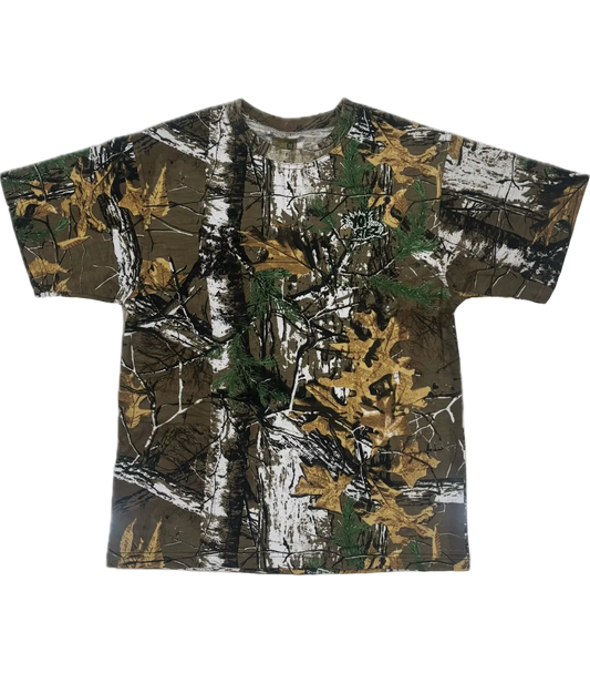 A short-sleeve crewneck t-shirt featuring a realistic woodland camouflage pattern with brown tree trunks, green pine needles, and golden-yellow autumn leaves on a white background.