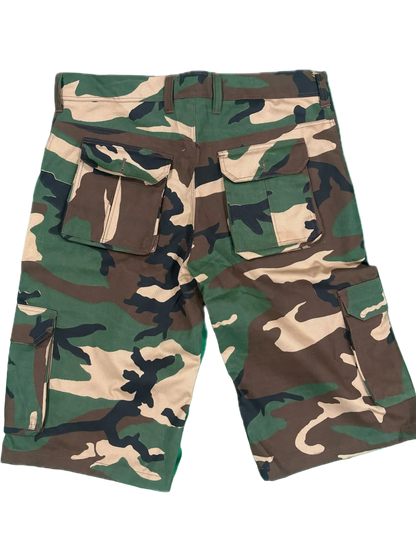 A pair of camouflage cargo shorts with green, brown, and beige woodland camo pattern, featuring multiple utility pockets.