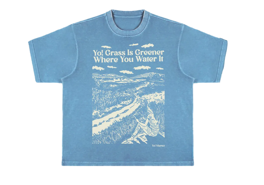 A blue crewneck t-shirt with a graphic print of a grassy field and the phrase 'Yol grass is greener where you water it'.