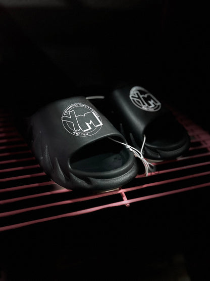 A pair of black slides with a white YM logo on the footbed